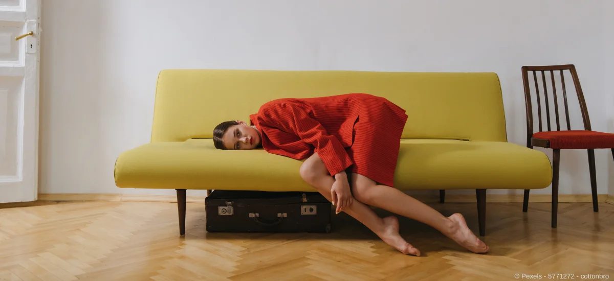 Eine Frau in roter Jacke liegt auf einer skandinavischer Couch 